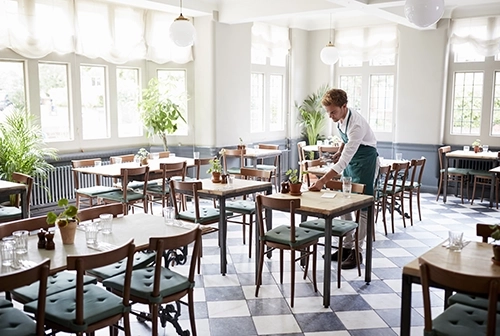 Joven poniendo a punto la sala del comedor de un restaurante