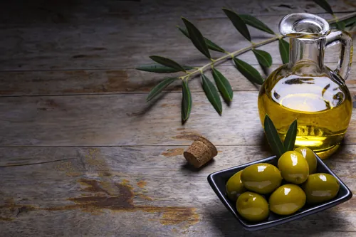 Aceite y aceitunas verdes dispuestos sobre una mesa de madera