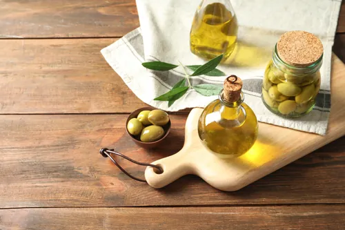 Aceite y aceitunas verdes presentados sobre un tablero de madera