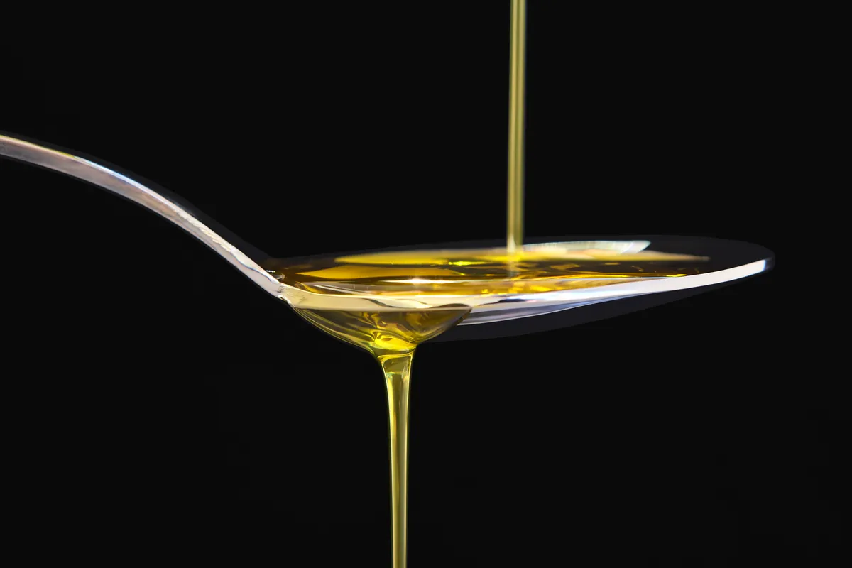 Chorro de aceite dorado cayendo sobre una cuchara metálica