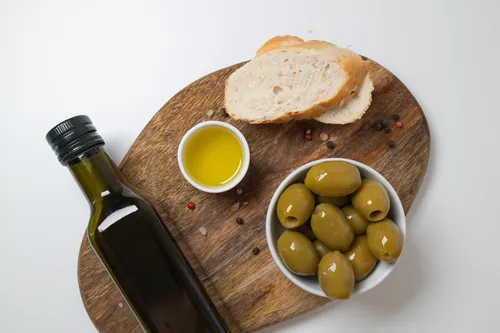 Cuenco con aceite ecológico rodeado de aceitunas verdes enteras