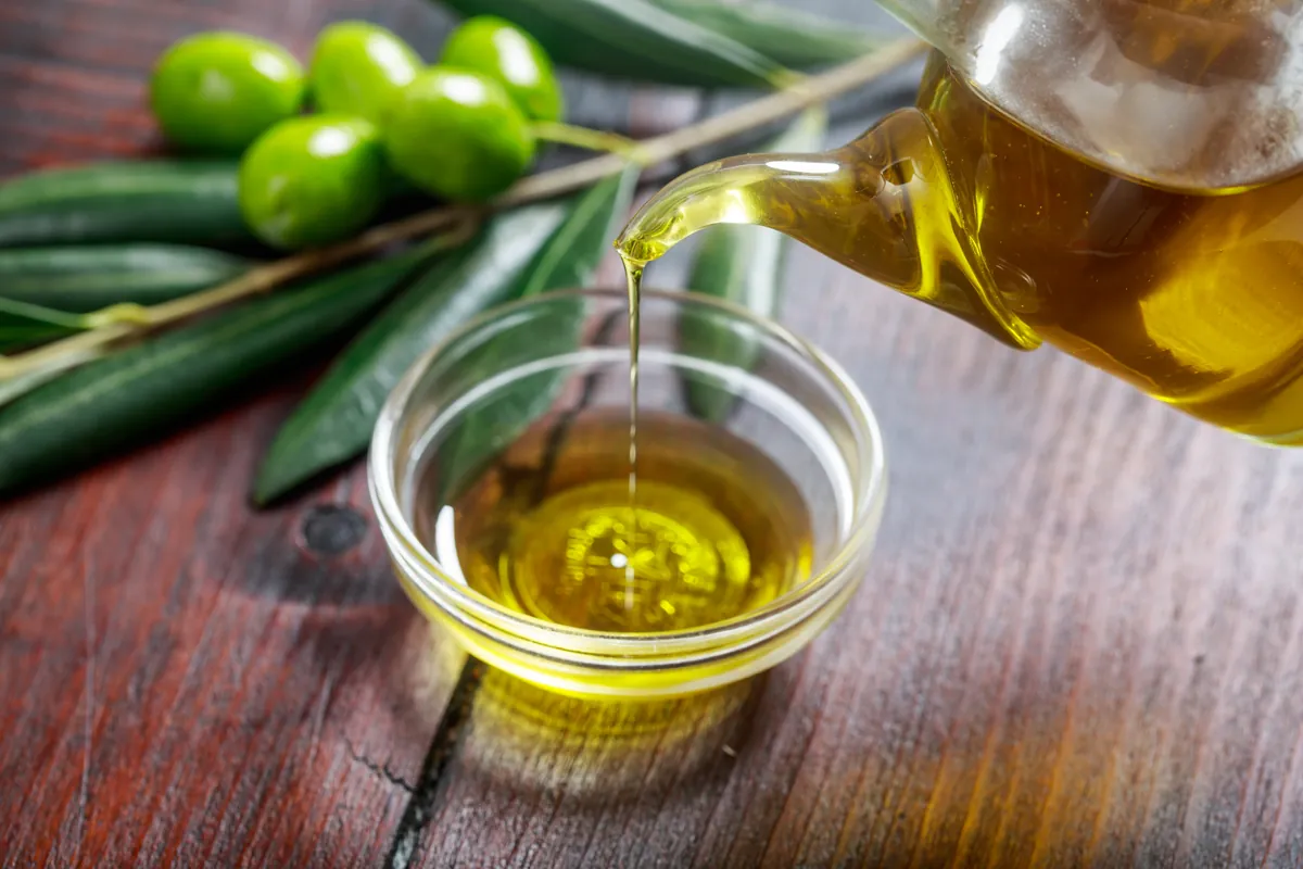 Aceite cayendo dentro de un cuenco con aceitunas verdes