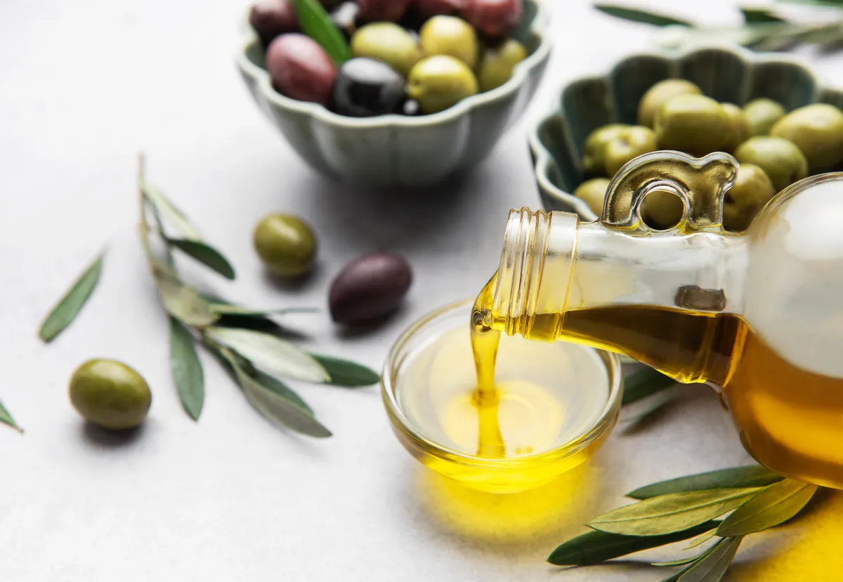 Chorro de aceite de oliva cayendo junto a aceitunas y ramas