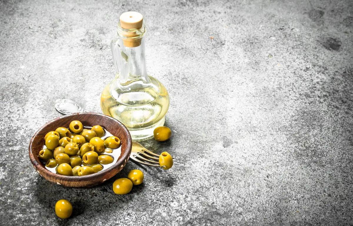 Aceitunas verdes y aceite sobre una superficie gris lisa