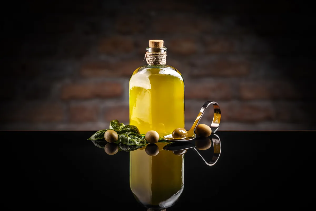 Aceitunas verdes colocadas junto a un recipiente con aceite
