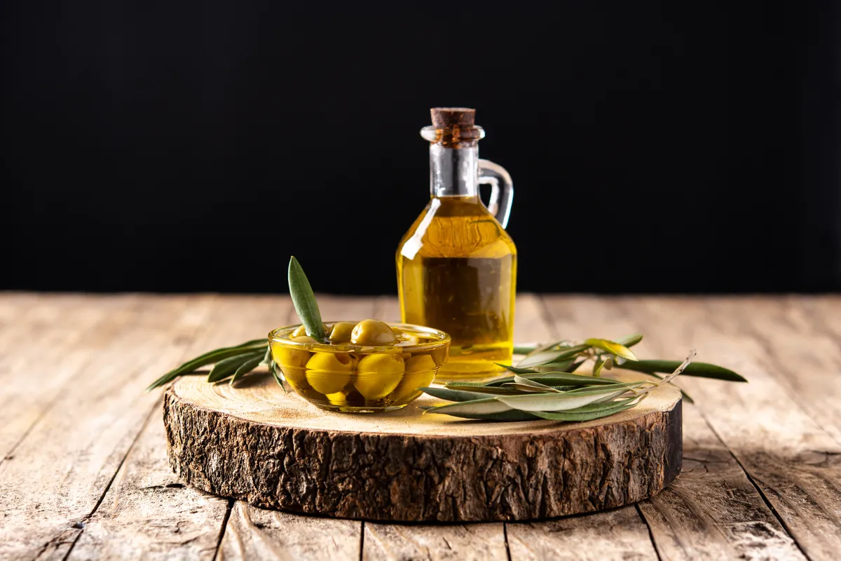 Botella de aceite virgen junto a unas aceitunas verdes
