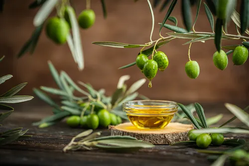 Cuenco de aceite con aceitunas verdes y hojas de olivo