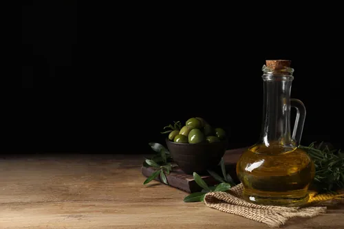Jarra de cristal con aceite rodeada de aceitunas y hojas