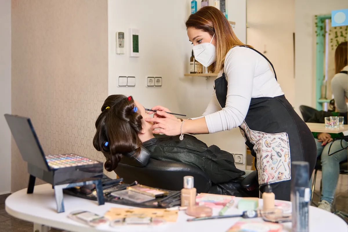 Maquilladora trabajando sobre el rostro de una clienta en cabina