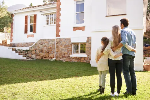 Familia abrazada mirando su nueva casa desde el jardín