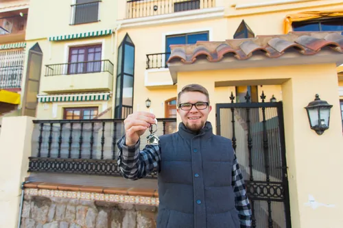 Hombre sosteniendo las llaves delante de una vivienda unifamiliar