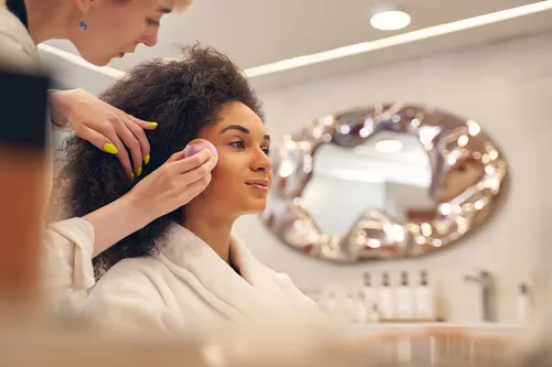 Estilista maquillando a una clienta sentada en el centro de estética